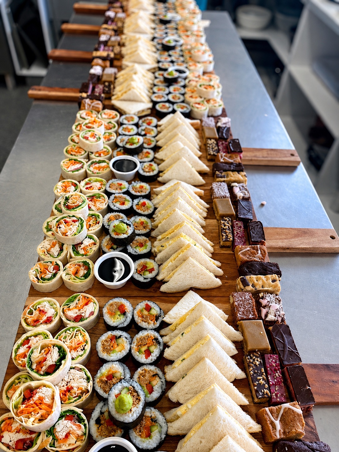 A long table of catering platters, sandwiches, sushi and slices from Beechwoods